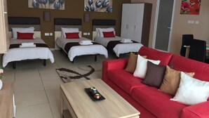Ein Hotelzimmer mit drei Betten, einem roten Sofa, einem Holztisch und Bildern an den Wänden.