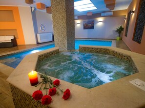Ein Whirlpool mit Kerze und Blumen, ein Schwimmbecken und ein Empfangsbereich mit einer Bank.