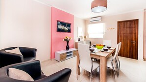 A modern living room with a pink accent wall, a dining area with a wooden table and chairs, and a large window providing natural light. - Green 2: Two-Bedroom Apartment in St. Julian's (Swieqi)