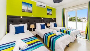 A hotel room with three beds, a bright green accent wall, and a view of the city. - Green 2: Two-Bedroom Apartment in St. Julian's (Swieqi)