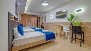 A hotel room with two beds, a desk, chairs, a flat-screen TV, and a potted plant. - Green 6: Studio Apartment in St. Julian's (Swieqi)