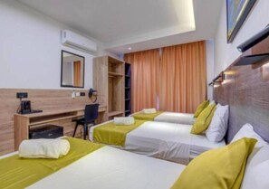 Een hotelkamer met drie eenpersoonsbedden, een bureau met stoel, een garderobe en een groot raam met gordijnen.
