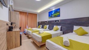 A hotel room with four single beds, each with a yellow bedspread and white pillows. There is a wooden desk with a kettle and a flat-screen TV mounted on the wall above the beds. - Green 11: Two-Bedroom Apartment in St. Julian's (Swieqi)