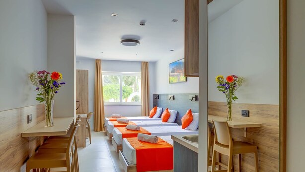 A hotel room with a long corridor, wooden furniture, and a bed with orange bedding. - Black 8: Studio Apartment in St. Julian's (Swieqi)