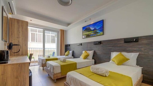 A hotel room with two beds, a wooden desk, a television, and a large window. - Red 5: Studio Apartment in St. Julian's (Swieqi)