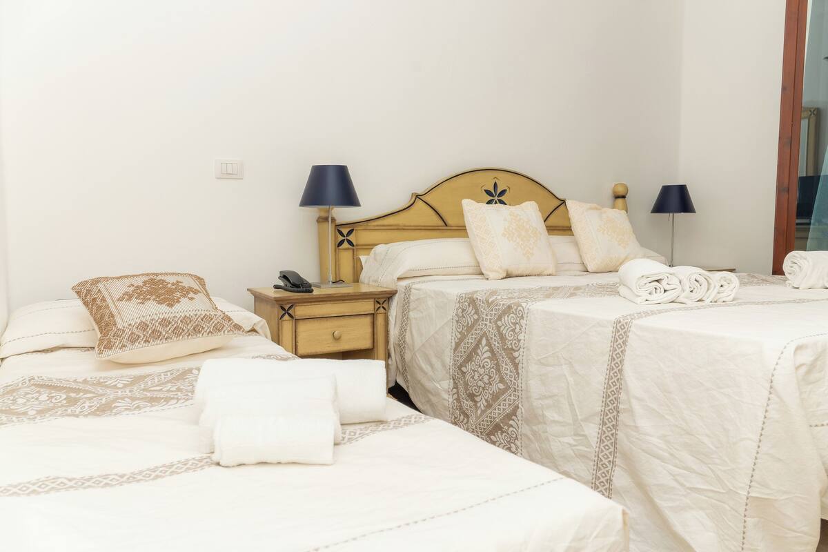 A hotel room with two beds, each with a headboard, bedside tables, lamps, and neatly folded towels.