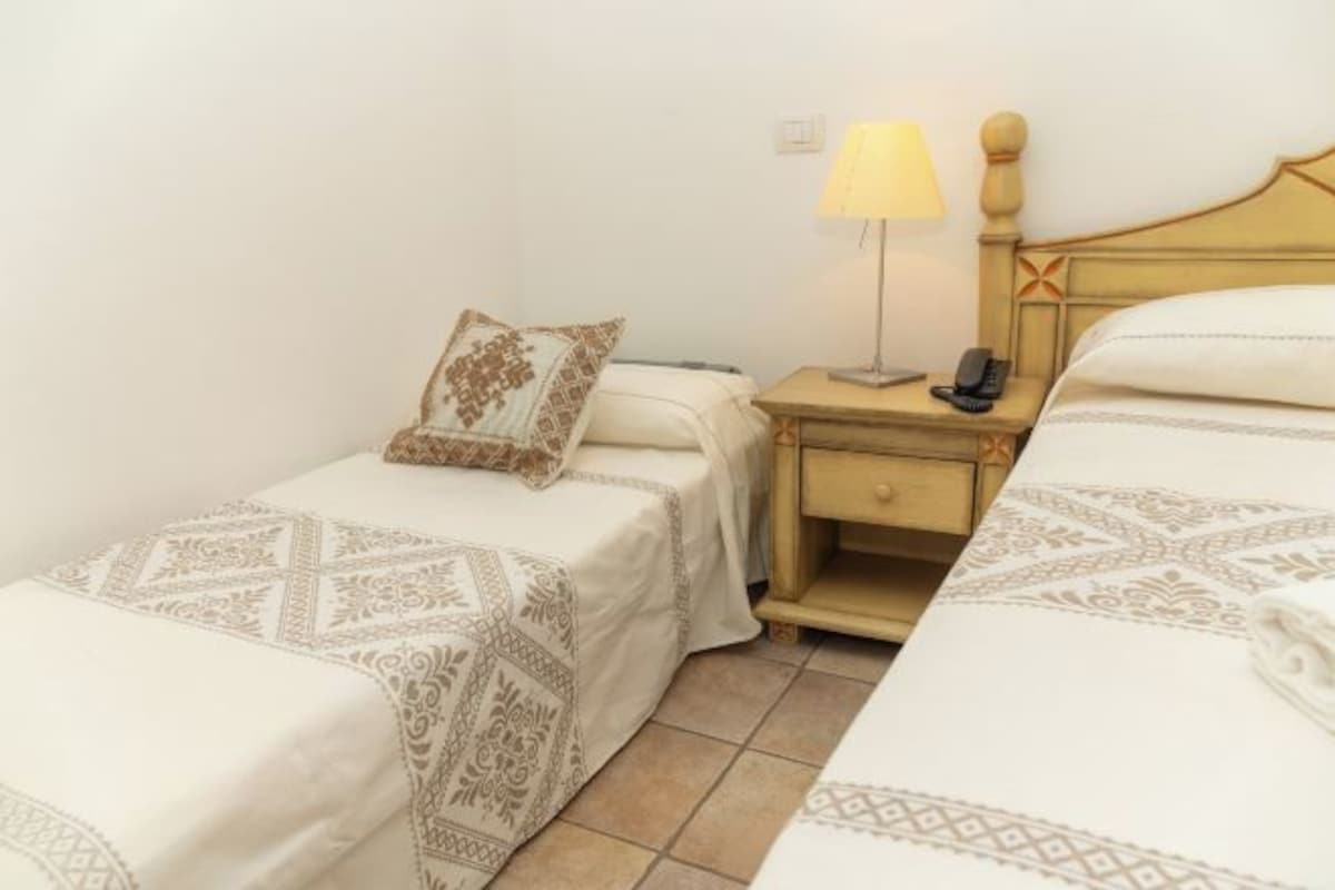 Une chambre d’hôtel avec deux lits simples, une table de chevet avec une lampe et un téléphone.