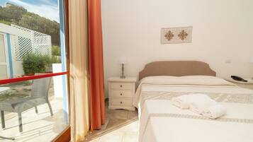 A hotel room with a bed, a nightstand, a lamp, a window with curtains, and a view of the outdoors.