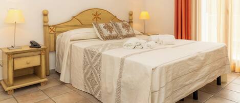 Una cama bien hecha con una colcha estampada, dos lámparas de noche, un teléfono junto a la cama y una mesita de noche de madera con un cajón.