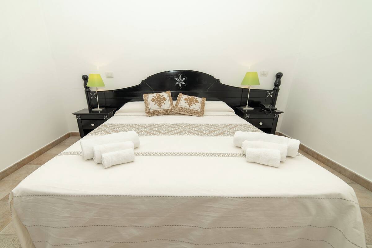 A neatly made bed with white linens and decorative pillows, flanked by two bedside tables with lamps.