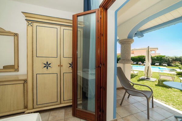 A room with a sliding glass door leading to a pool area, a beige wardrobe, and a chair by the window.