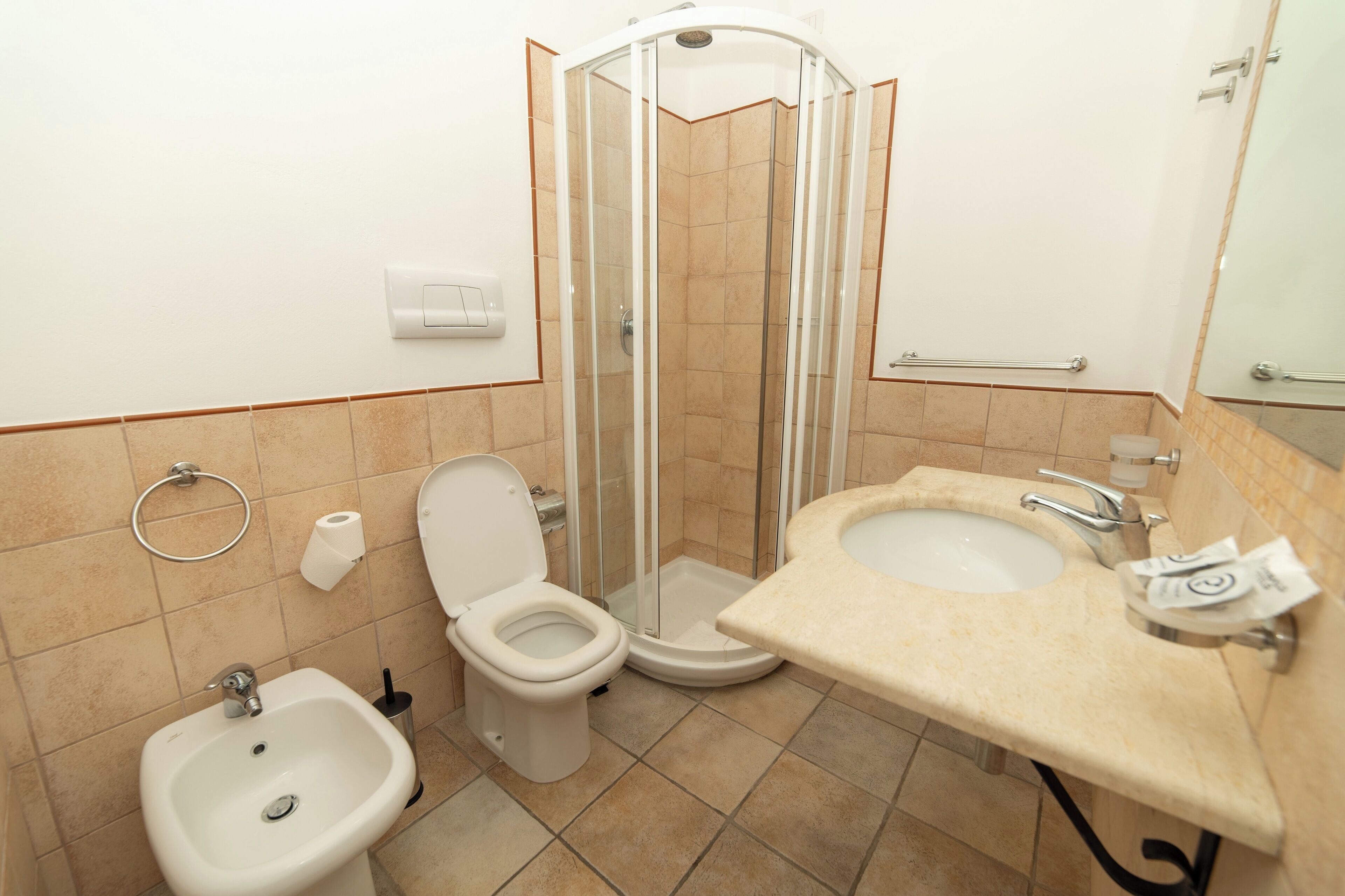 A bathroom with a toilet, bidet, sink, and a glass-enclosed shower.