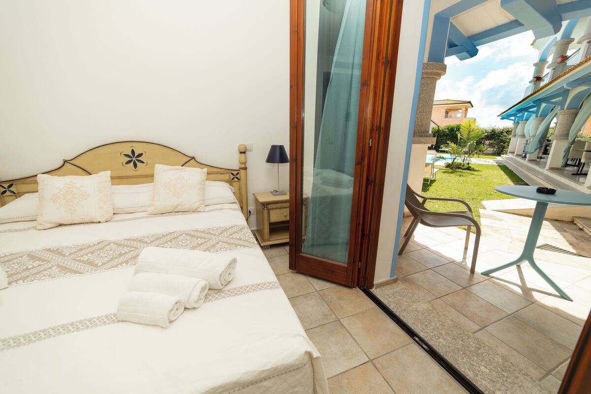 A hotel room with a bed, a desk, and a view of a pool and garden.