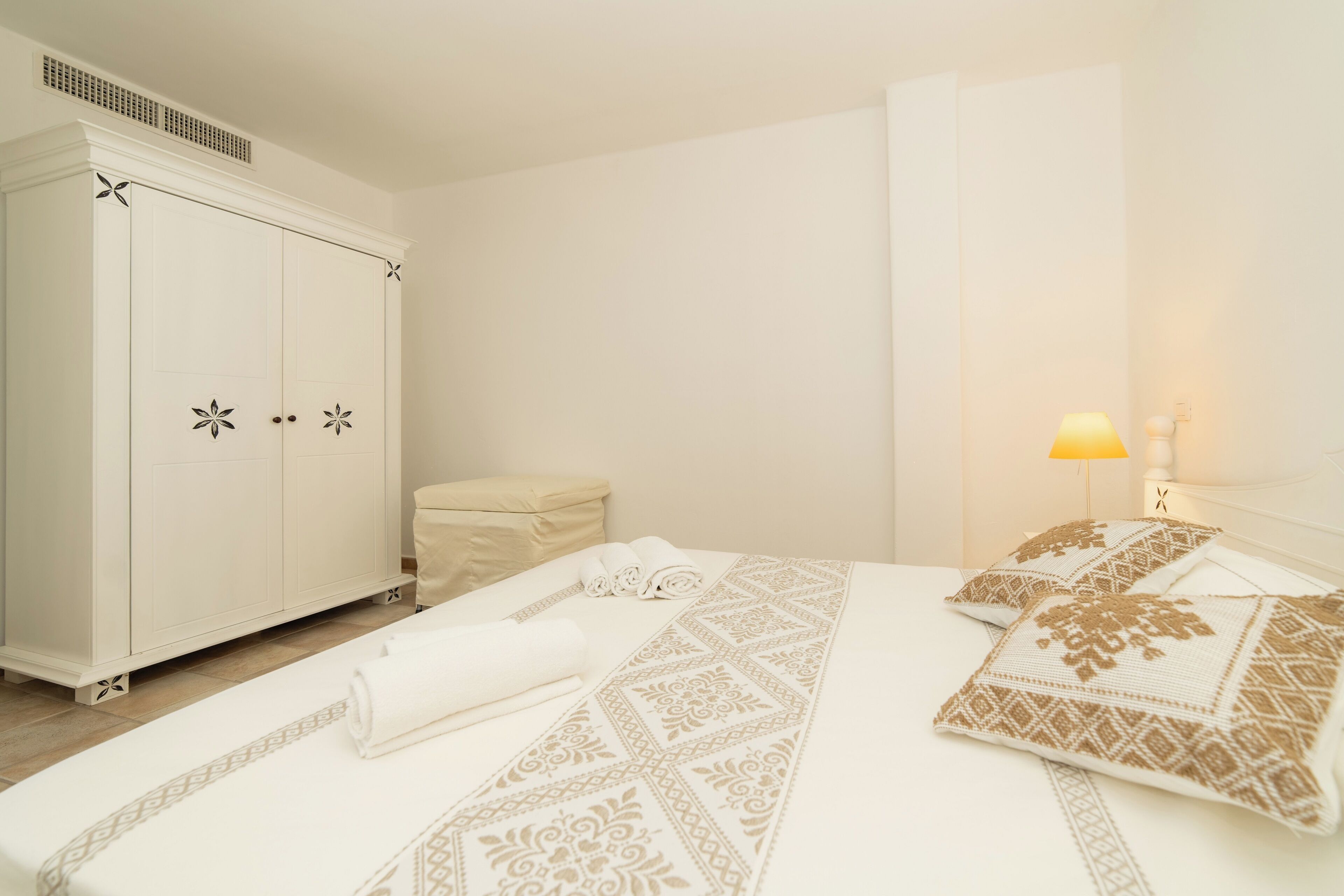 Une chambre d’hôtel avec une grande armoire, un lit avec une literie à motifs, une lampe de chevet et une petite table de chevet.