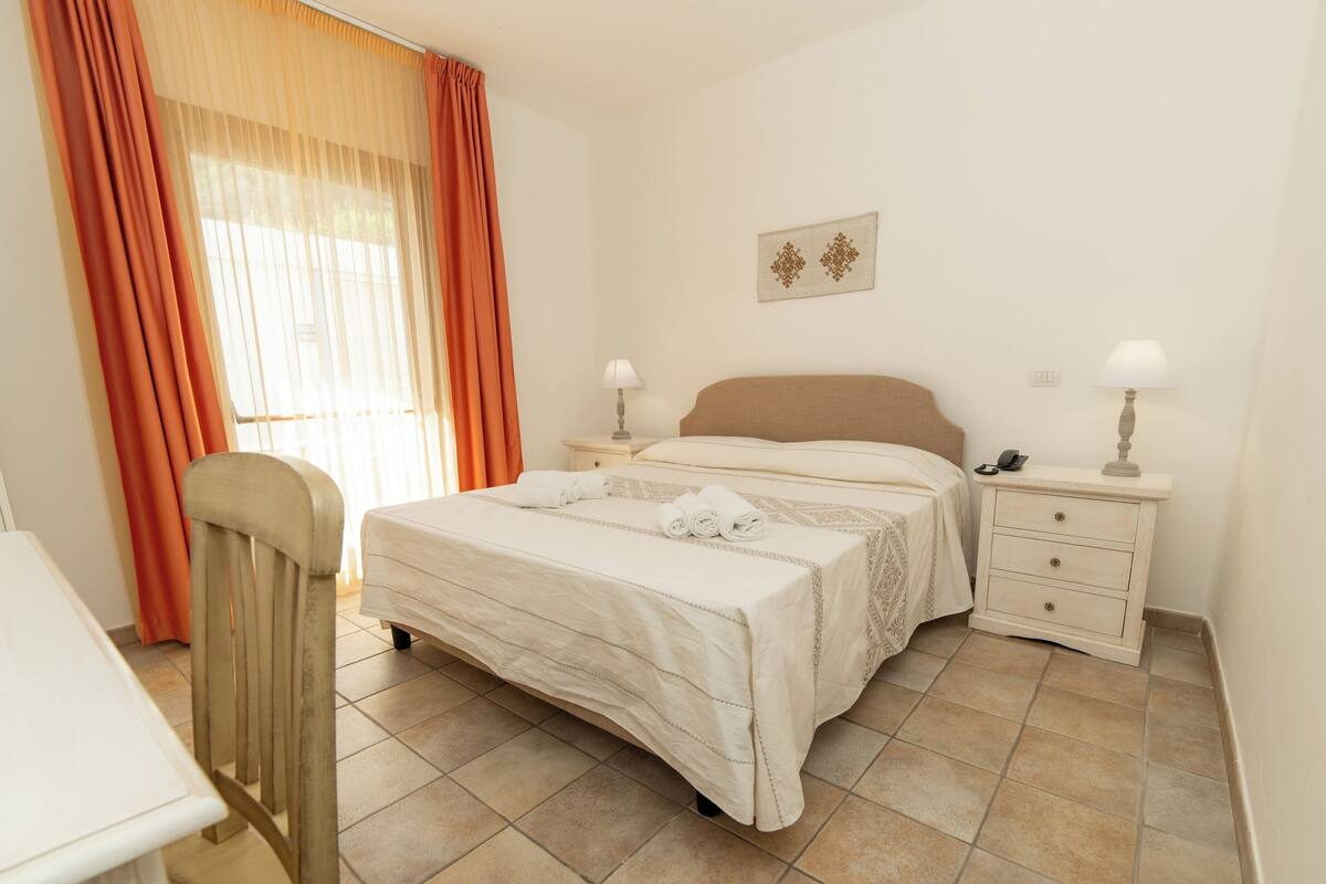 A bedroom with a bed, two bedside tables, a chair, and a window with curtains.