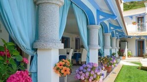 Un hotel con un área exterior techada que cuenta con columnas, plantas en macetas y un césped bien cuidado.