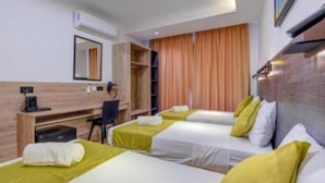 Une chambre d’hôtel avec trois lits simples, un bureau avec une chaise, une armoire et une grande fenêtre avec des rideaux.