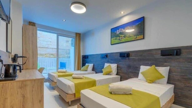 Une chambre d’hôtel avec trois lits, un bureau en bois et une grande fenêtre.