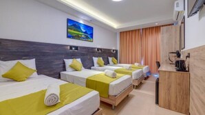 Une chambre d’hôtel avec trois lits, un bureau et un tableau au mur.