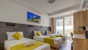 Une chambre d’hôtel avec trois lits, un bureau en bois et une grande fenêtre.
