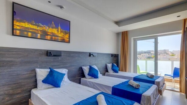 A hotel room with three beds, a cityscape painting, and a balcony with a view. - Blue 6: Studio Apartment in St. Julian's (Swieqi)