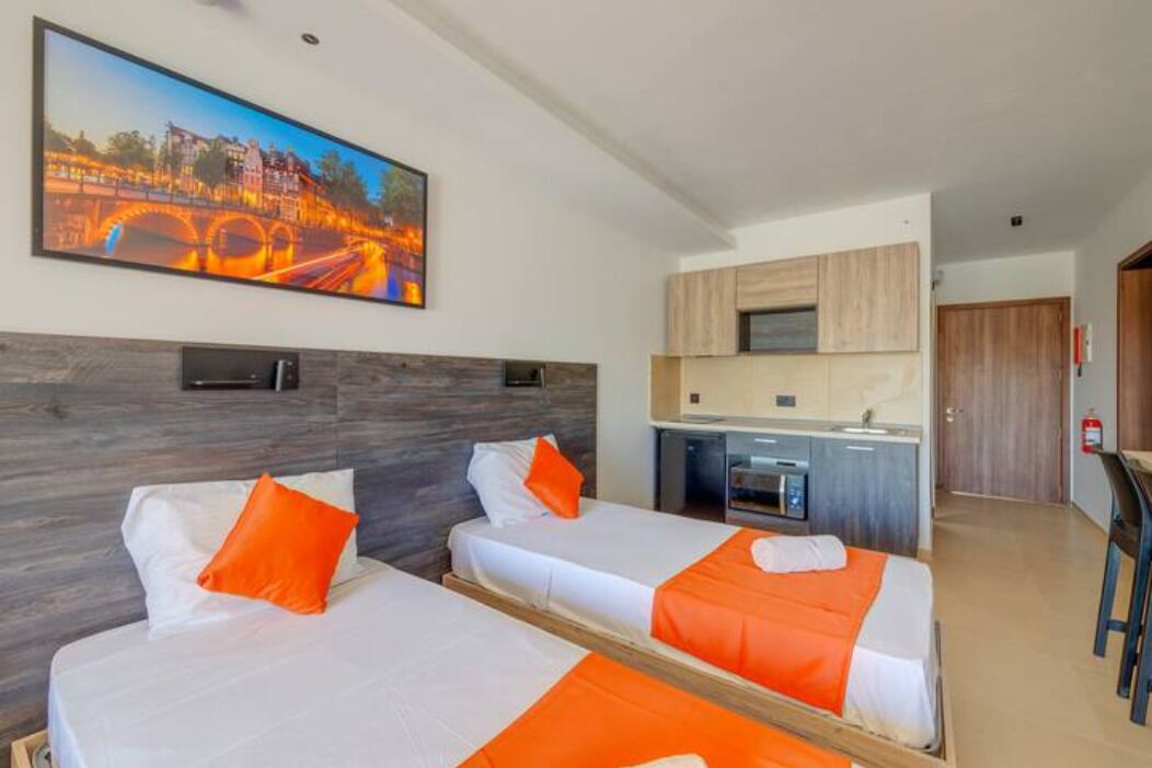 Quarto de hotel com duas camas, uma kitchenette e uma pintura de uma ponte.