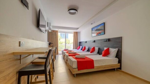 Een hotelkamer met een houten bureau, een bed met rode kussens en een televisie aan de muur.