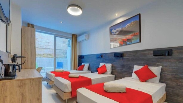 Hotellihuone, jossa on kolme sänkyä, puinen työpöytä ja suuri ikkuna.