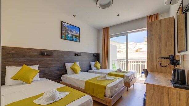 Une chambre d’hôtel avec deux lits, une tête de lit en bois, un tableau, un balcon et une kitchenette.