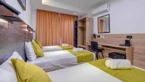 Une chambre d’hôtel avec trois lits, un bureau, une chaise et une armoire.