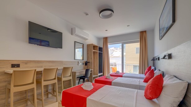 A hotel room with two beds, a desk, chairs, a TV, and a window with curtains.