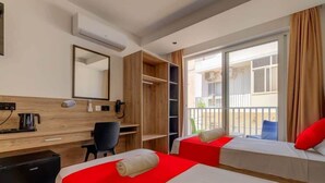 A hotel room with two beds, a desk, a chair, and a view of the outside balcony.