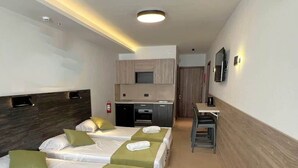Een hotelkamer met drie bedden, een kitchenette, een bureau en een spiegel.