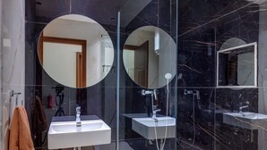 Een moderne badkamer met twee wastafels, een douchecabine met glazen wanden en grote spiegels.