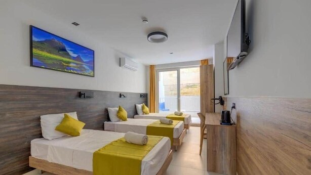 A hotel room with three beds, a TV, and a painting on the wall. - Yellow 13: Two-Bedroom Apartment in St. Julian's (Swieqi)