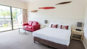 Camera d'albergo con un letto grande, una poltrona rossa, un comodino e vista sull'esterno.