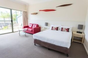 Habitación de hotel con una cama grande, un sillón rojo, una mesita de noche y vistas al exterior.