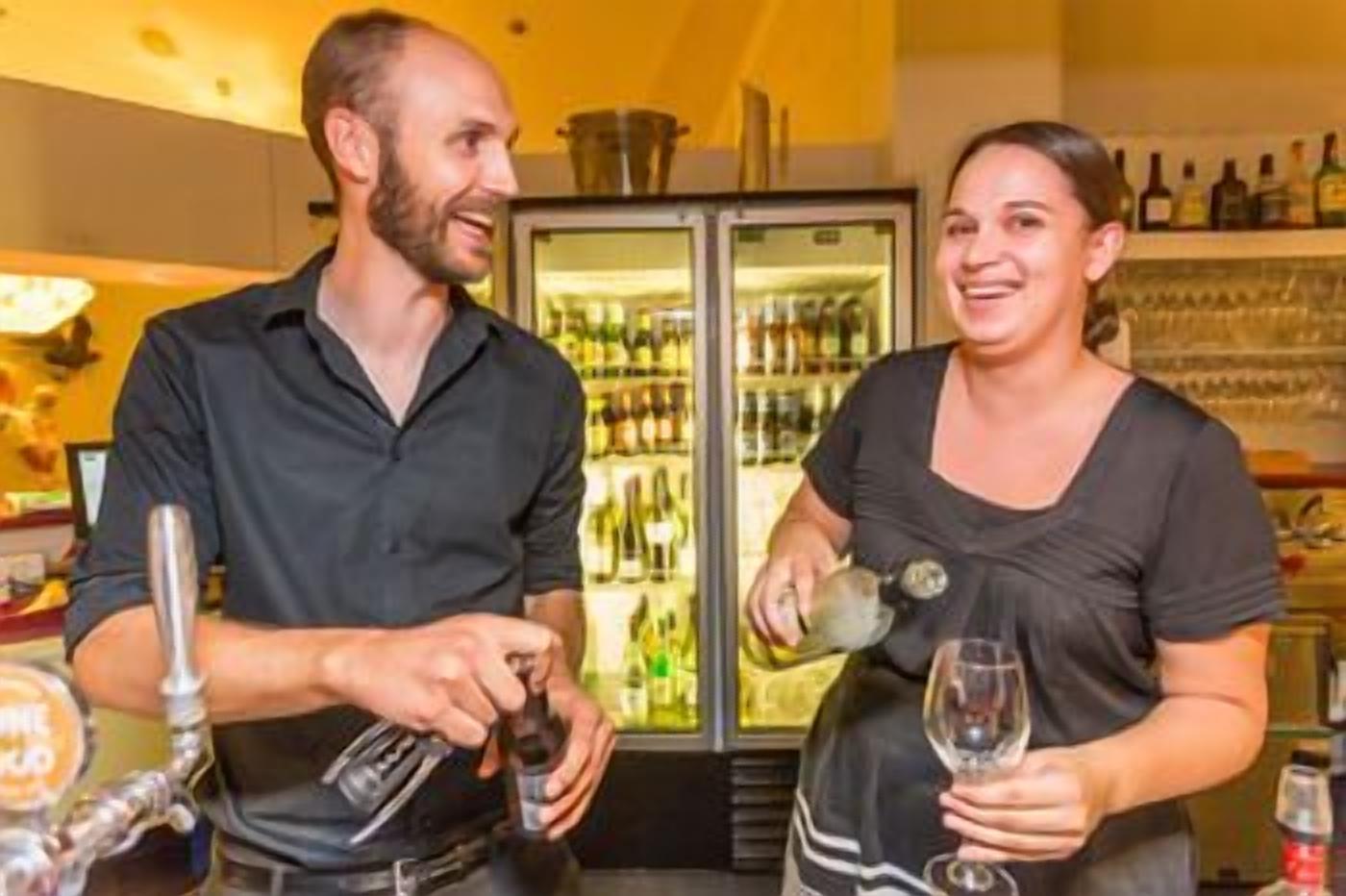 A bar area with a person pouring a drink and another holding a glass.