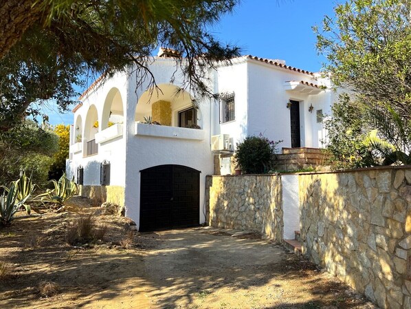 A white building with a stone wall, a black garage door, and a paved driveway.