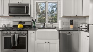A modern kitchen with a stove, microwave, oven, dishwasher, and a window with a view of trees. - Lakefront 3-BR Retreat in the Berkshires (Becket)