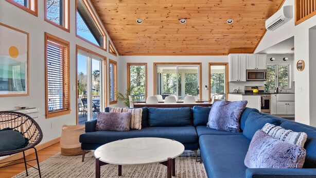 A modern living room with a sectional sofa, a round coffee table, and a dining area with a table and chairs. - Lakefront 3-BR Retreat in the Berkshires (Becket)