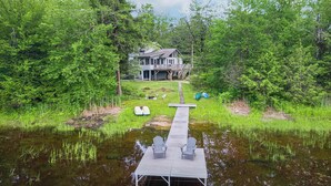 A lakeside cabin with a dock extending into the water, surrounded by dense forest. - Lakefront 3-BR Retreat in the Berkshires (Becket)