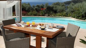 A dining table with breakfast items and a view of a pool and mountains. - Amapola Villas - Private Villas Phos & Agapi (Lefkada)