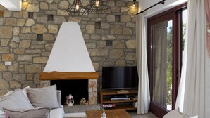 A living room with a stone fireplace, a flat-screen TV, and a sofa. - Amapola Villas - Private Villas Phos & Agapi (Lefkada)