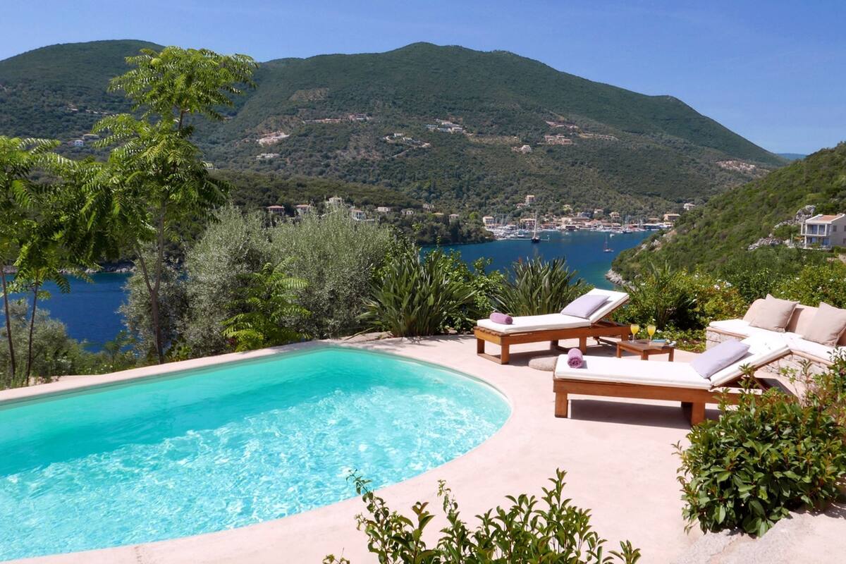Une piscine dotée de chaises longues, offrant une vue sur une ville côtière et les montagnes.