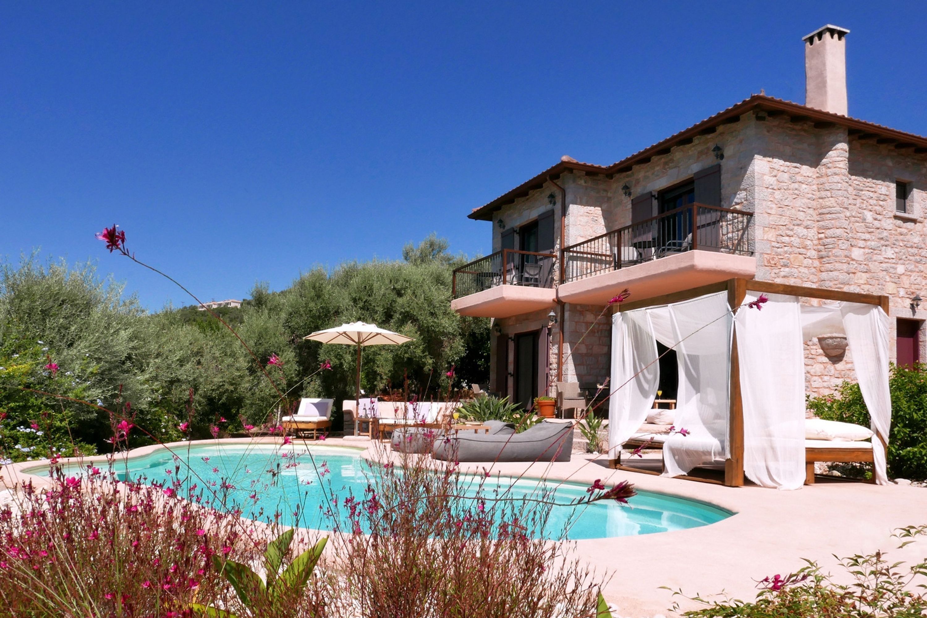 A stone villa with a pool, outdoor seating, and a covered area with canopies.