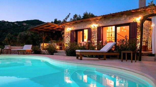 A poolside area with lounge chairs, a stone building with windows, and a view of a hillside. - Amapola Villas - Private Villas Phos & Agapi (Lefkada)