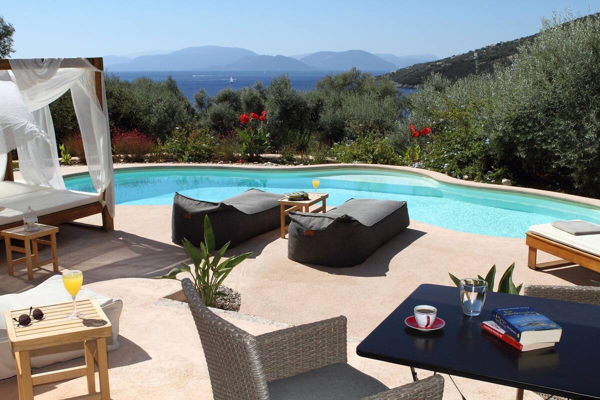 Un espace aménagé au bord de la piscine, avec un lit, des chaises longues et une table où sont disposés des boissons et des livres.