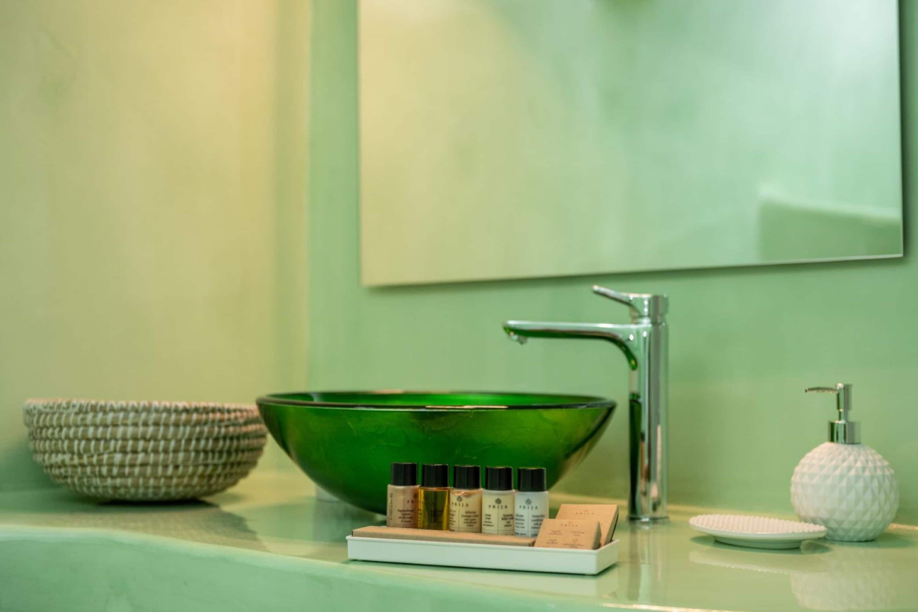 A bathroom with a green bowl sink, a white soap dispenser, and a tray with several bottles.