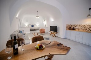 Ein modernes Interieur mit Esstisch, Weinflasche und Gläsern, einer Couch, einem Fernseher und einer Küchenzeile.